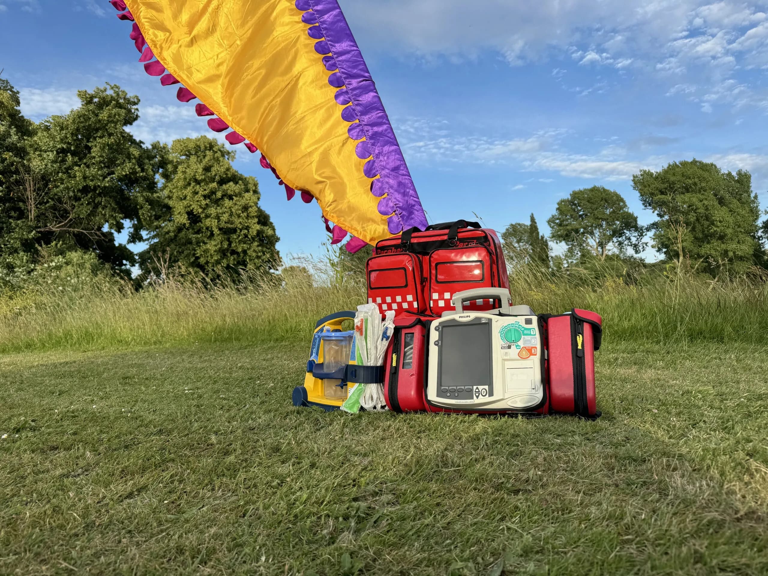 Medical response bags, an AED and oxygen equipment set up on grass at an outdoor event site.