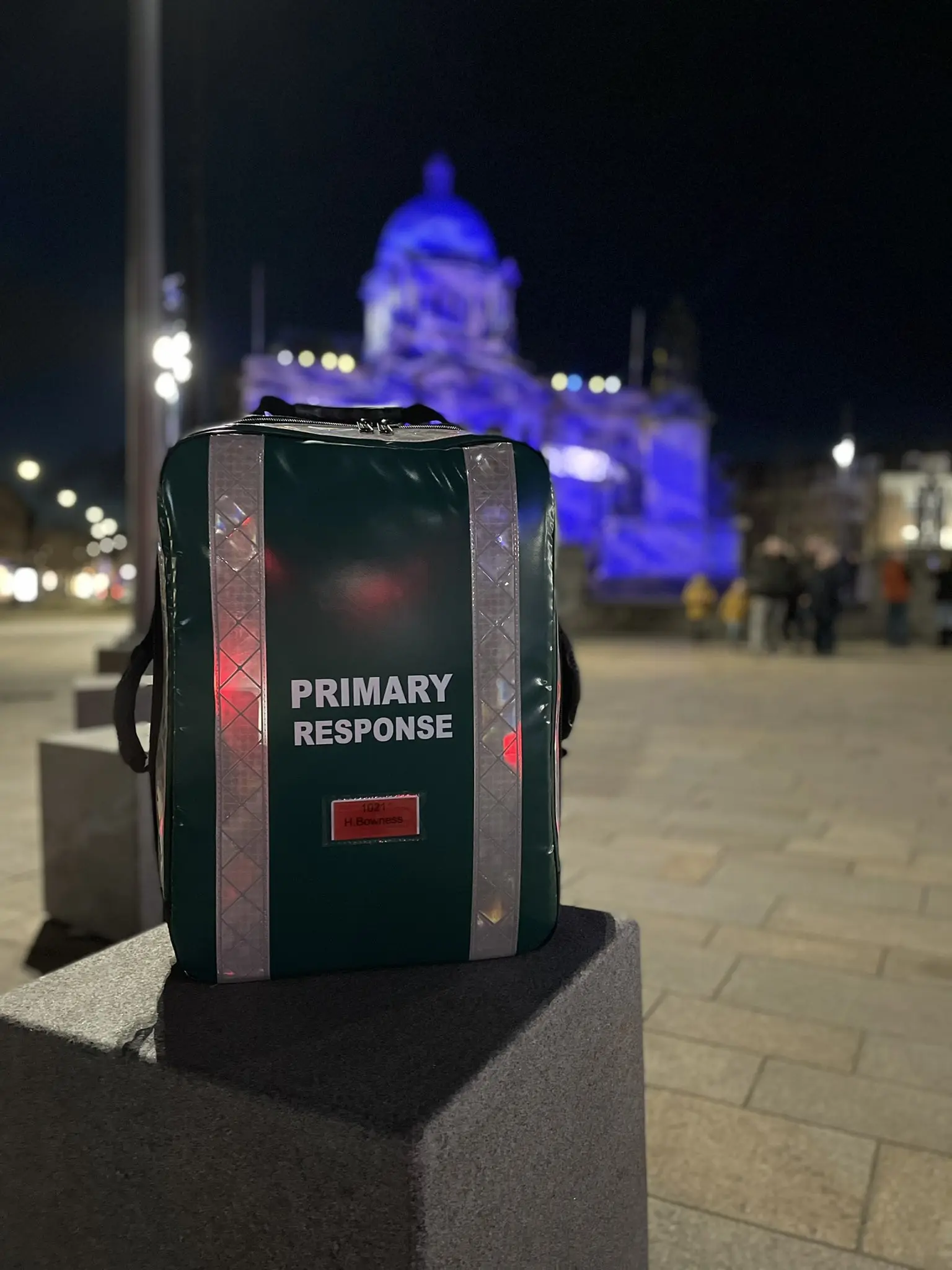 Primary response medical bag positioned in a city centre at night, with a lit civic building in the background.