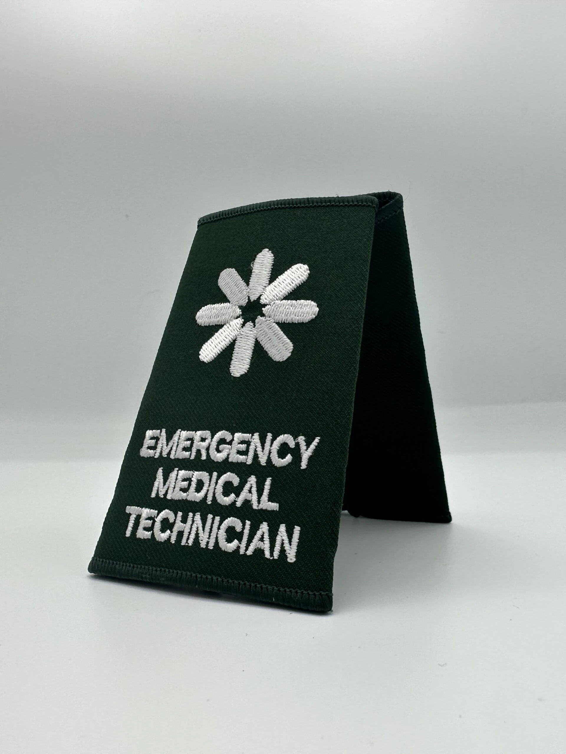 Two epaulettes back to back, embroidered with the words "Emergency Medical Technician", a type of clinical used for event medical cover.